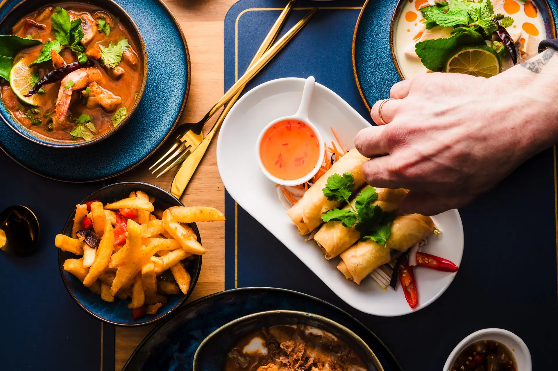 A table of Thai food: tom yum soup, spring rolls and sides