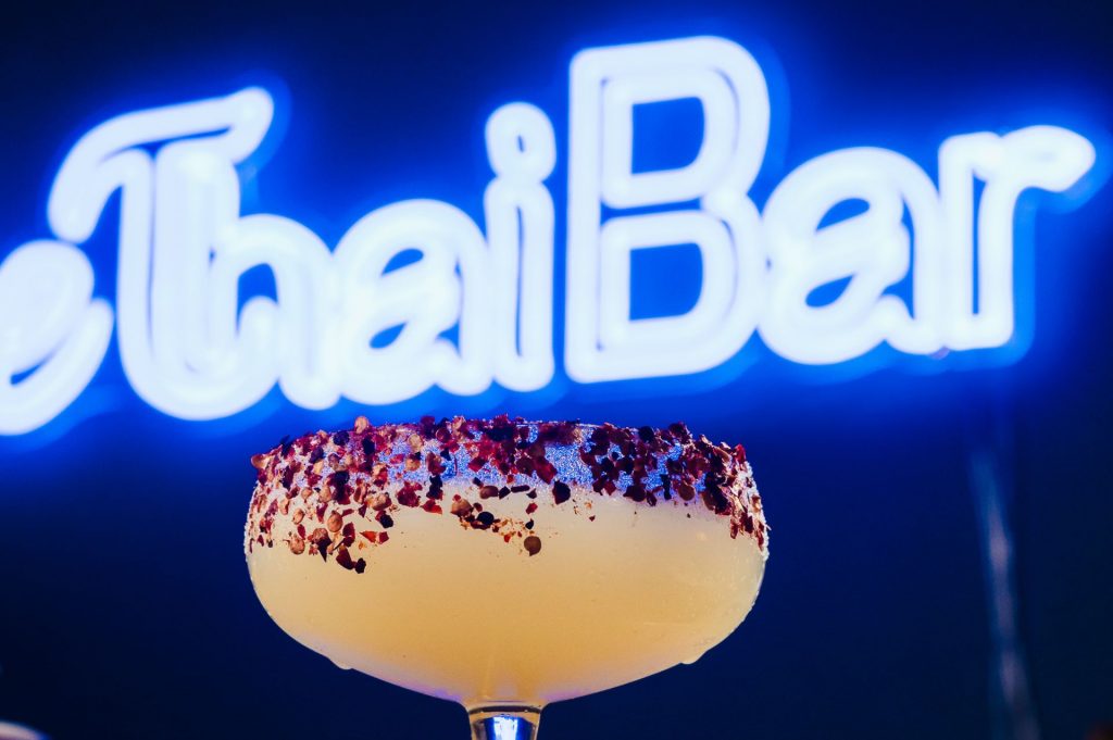 Thai cocktail with a neon sign saying Thai Bar in the background