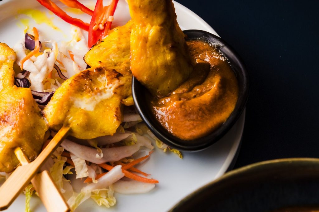 dipping chicken satay skewers into peanut sauce